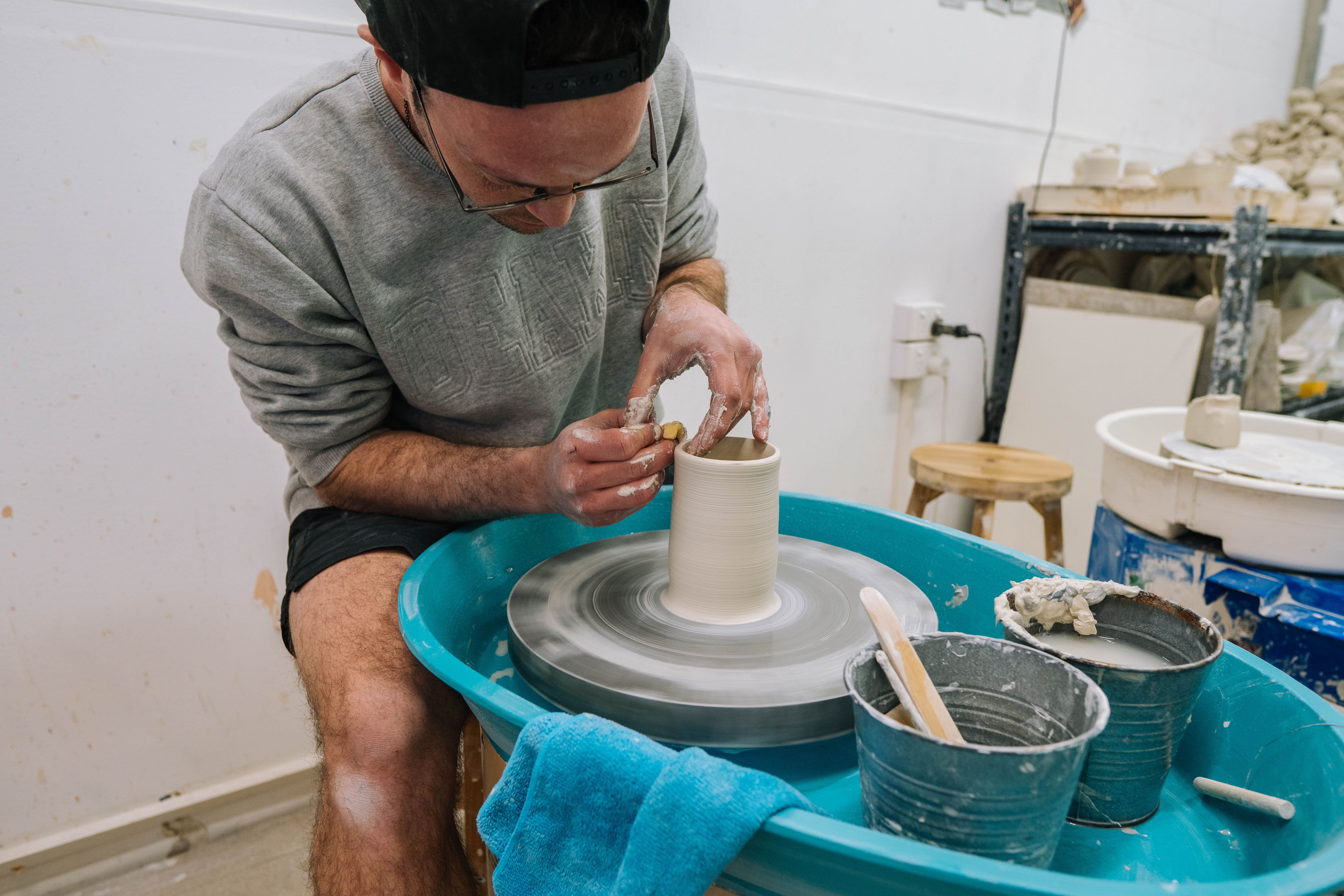 A man sitting at a potter's wheel forming clay into a shape